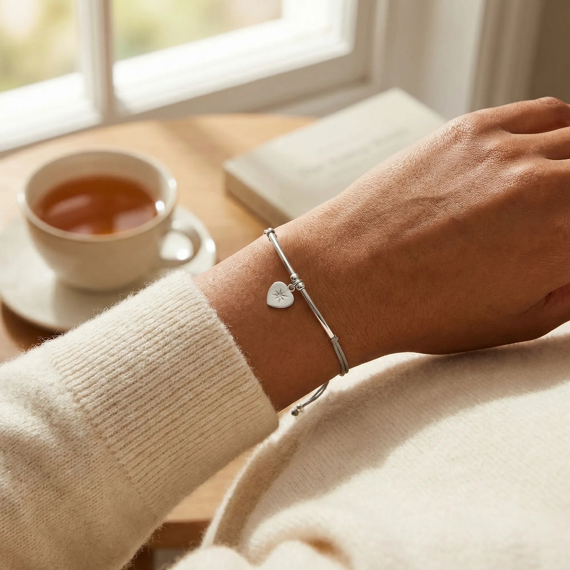 North Star heart silver bracelet on the wrist beside a cup of tea, casual weekend styling, Dubai DIFC UAE