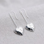 Open heart hammered 925 sterling silver long drop earrings on woven linen fabric, available in Dubai.