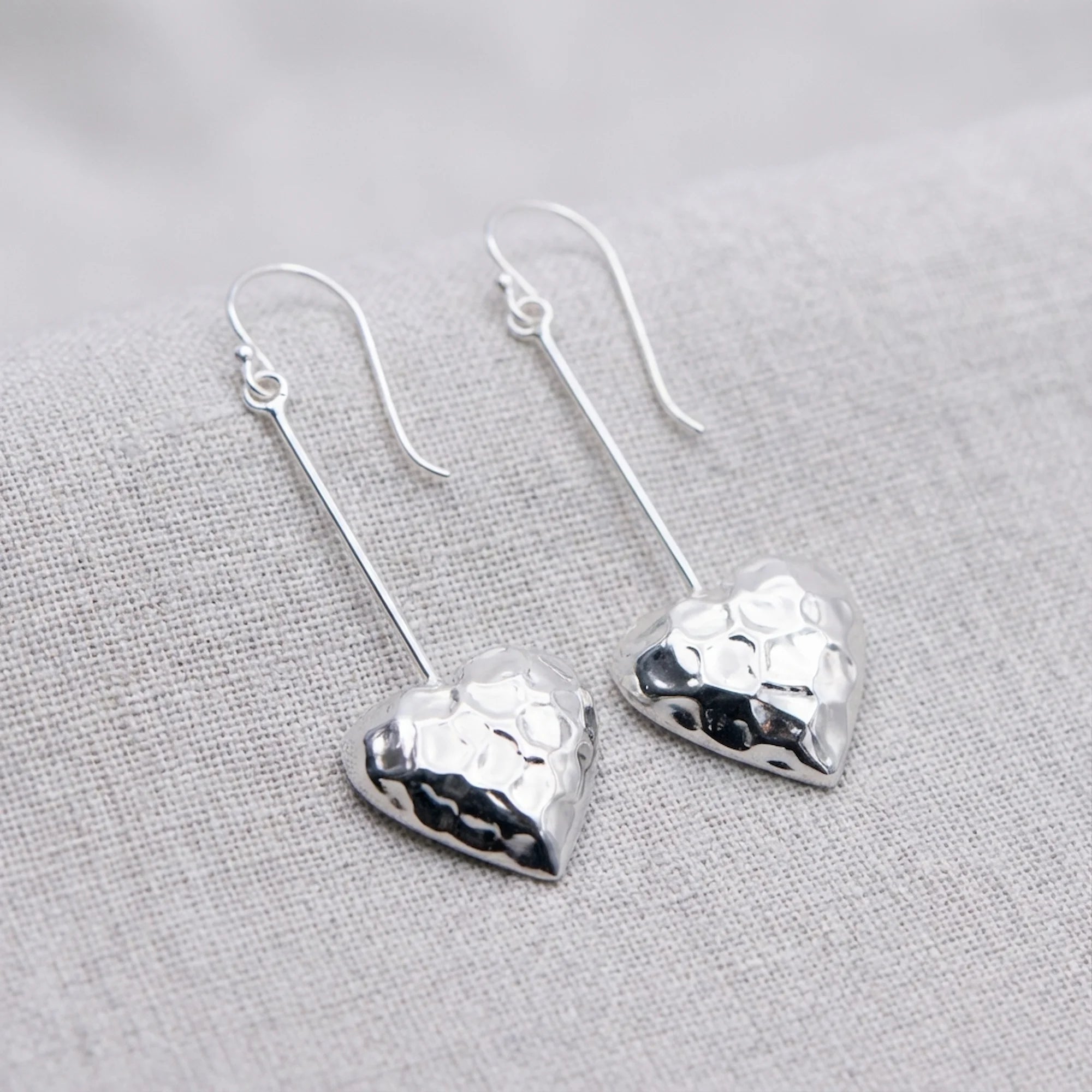 Open heart hammered 925 sterling silver long drop earrings on woven linen fabric, available in Dubai.