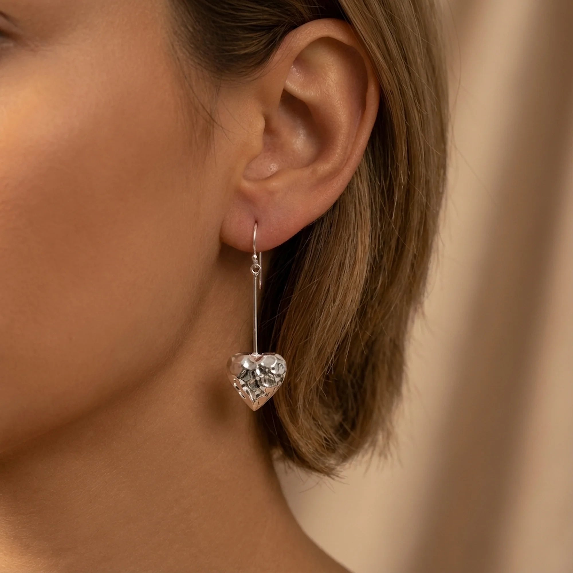Close view of a woman wearing open heart hammered 925 sterling silver drop earrings indoors in Dubai.