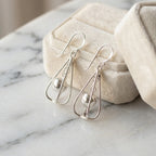 Silver orb drop earrings leaning against open Luna Dura cream velvet gift box on white marble surface