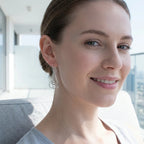  Close portrait of woman wearing silver framed orb drop earrings with Dubai Marina towers visible behind