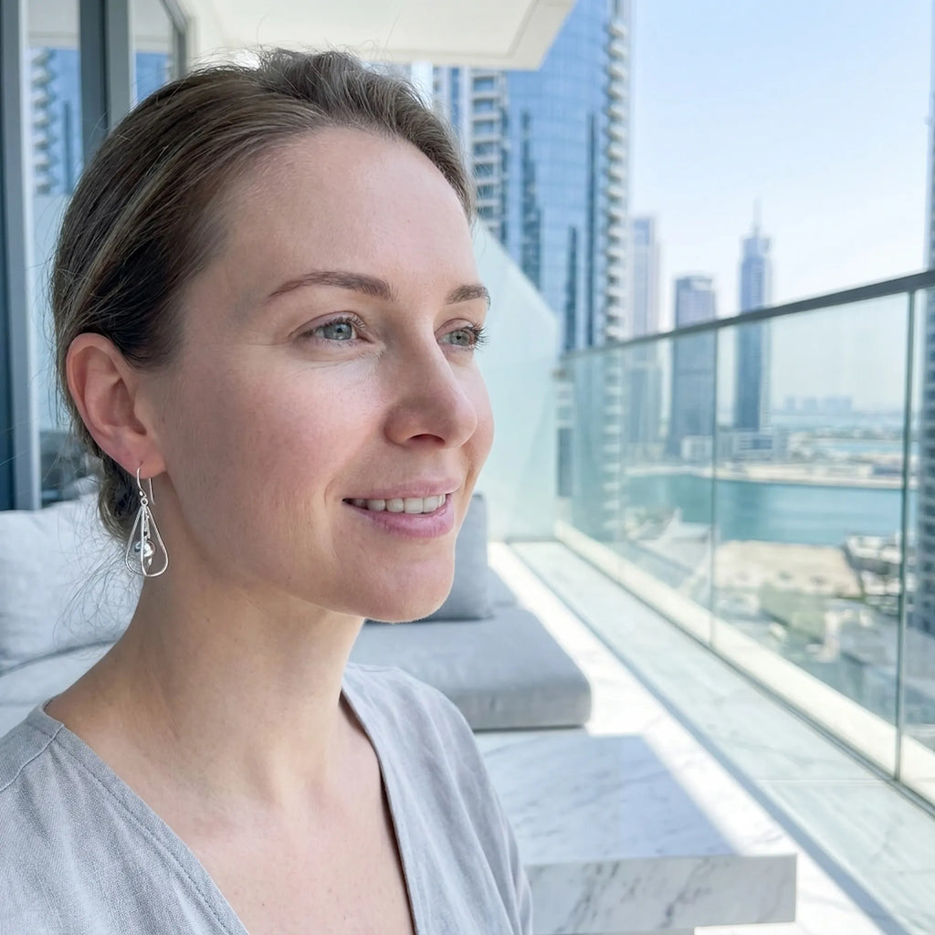Woman wearing silver orb drop earrings on balcony overlooking Dubai Marina skyline and waterway