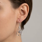 Side close-up of ear wearing silver kinetic orb drop earring showing suspended sphere inside open wire frame