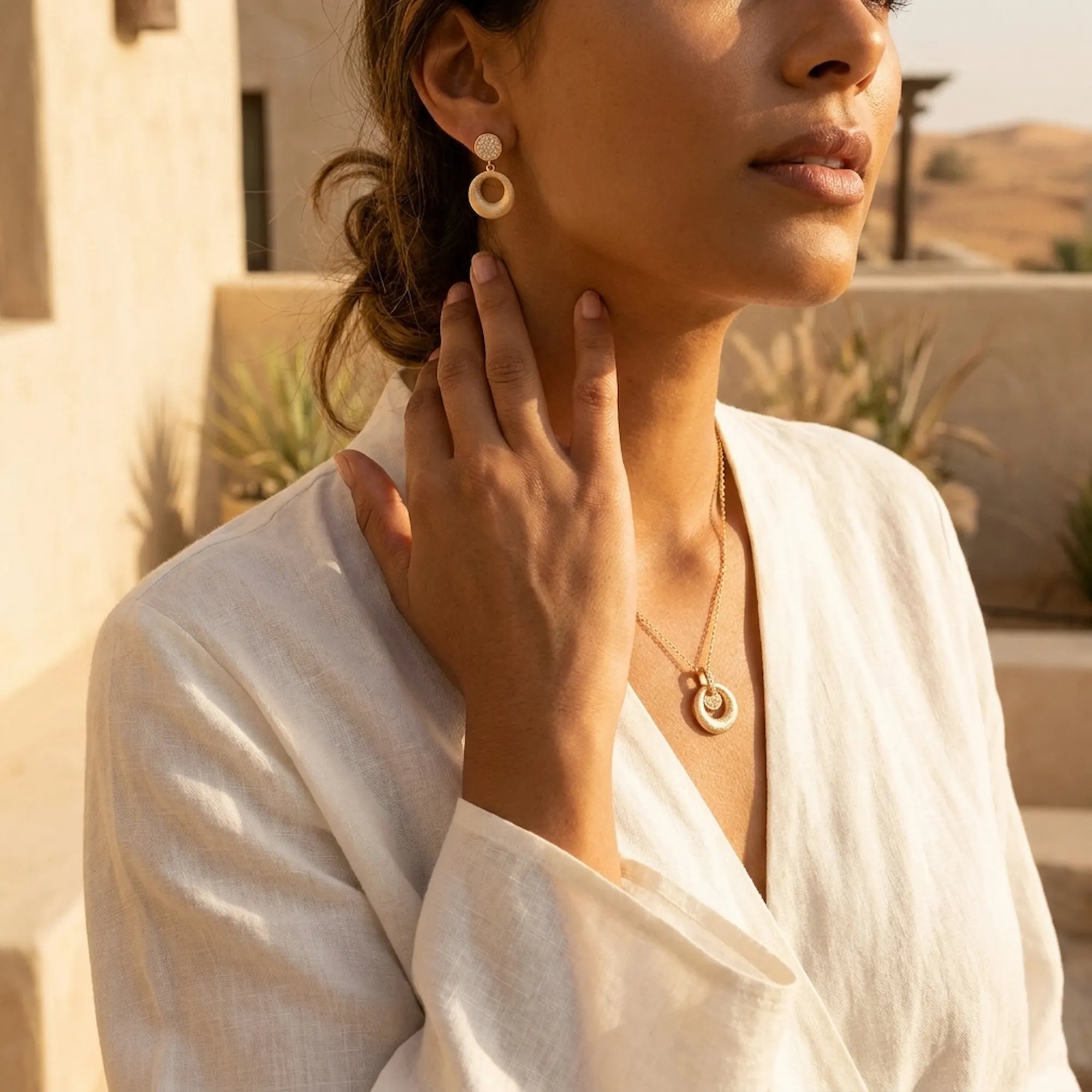 Dual circle pendant necklace and drop earrings worn on olive skin against UAE desert architecture — 18K gold set