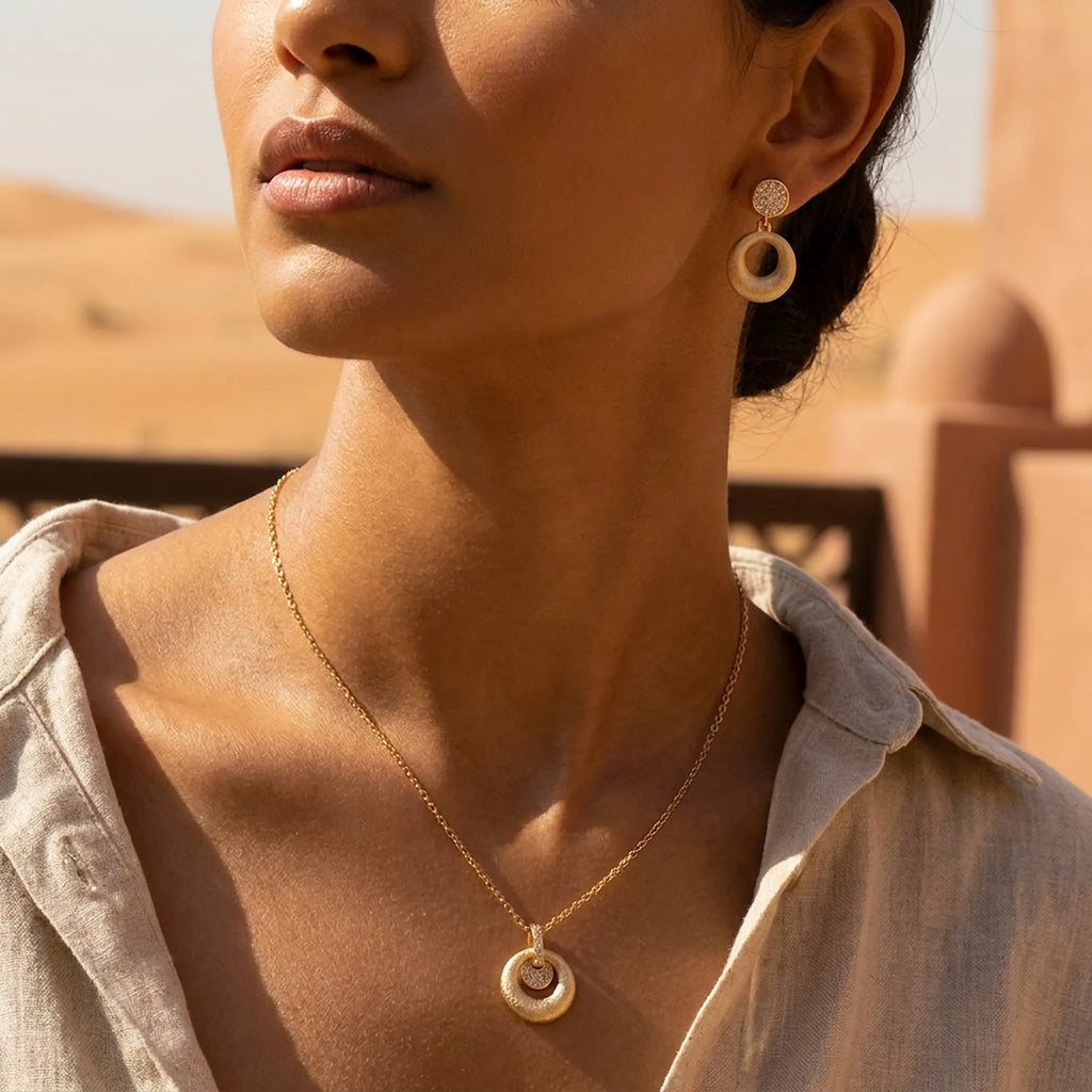 Matte ring and floating disc drop earrings and pendant in 18K gold worn in desert UAE setting — olive skin model