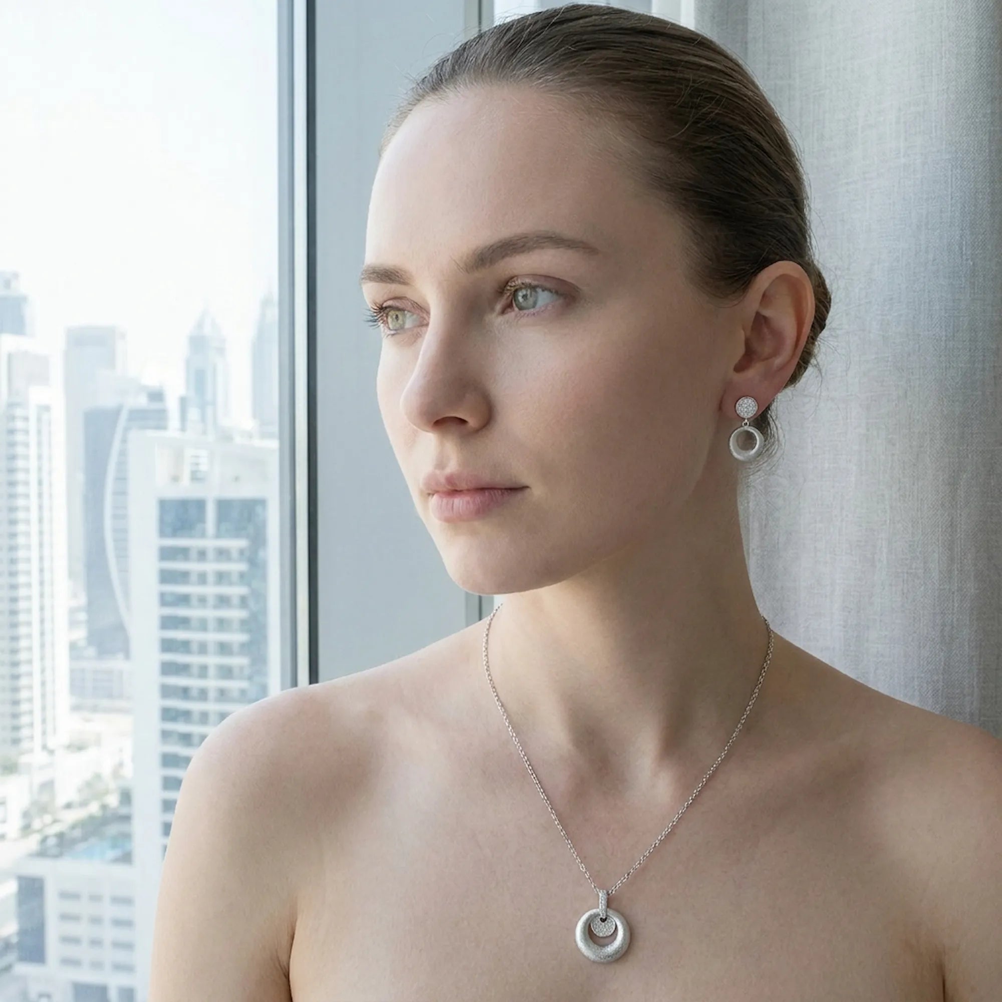 Rhodium silver circle disc earrings and pendant set worn by fair skin model — Dubai skyline through window