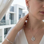 Rhodium silver circle pendant necklace and drop earrings worn with white top against modern UAE architecture