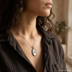 Woman wearing an oval Allah pendant with a satin silver centre and polished frame; styling chain not included.