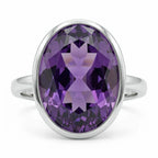 Macro close-up of a deep purple oval cut amethyst highlighting its internal faceting and the seamless silver bezel edge.