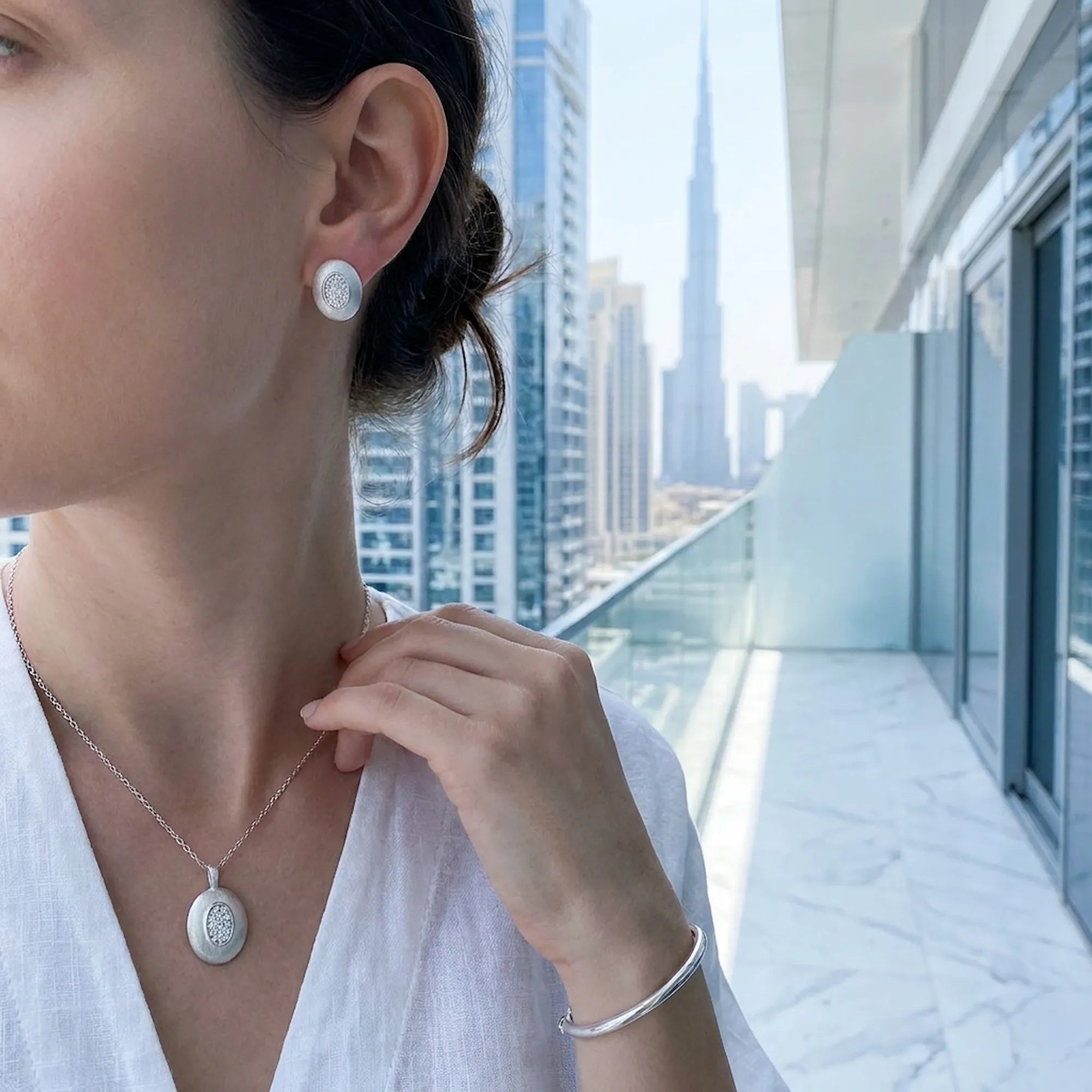 Rhodium silver oval pendant necklace and stud earrings worn with Burj Khalifa in background — Luna Dura Dubai