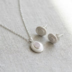 Rhodium silver oval pendant necklace and stud earrings on linen — brushed 925 sterling silver with CZ pavé centre