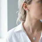 Brushed silver oval pendant necklace and stud earrings on fair skin model with white linen shirt — 925 sterling silver