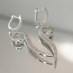 Both paved serpent drop earrings on reflective surface — huggie clicker open, green zircon CZ eyes and baguette spine detail