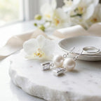 Silver pearl and rectangular cubic zirconia drop earrings beside a white orchid on marble