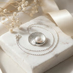 Pearl vortex pendant necklace on white marble with gypsophila and ribbon, showing lobster claw clasp