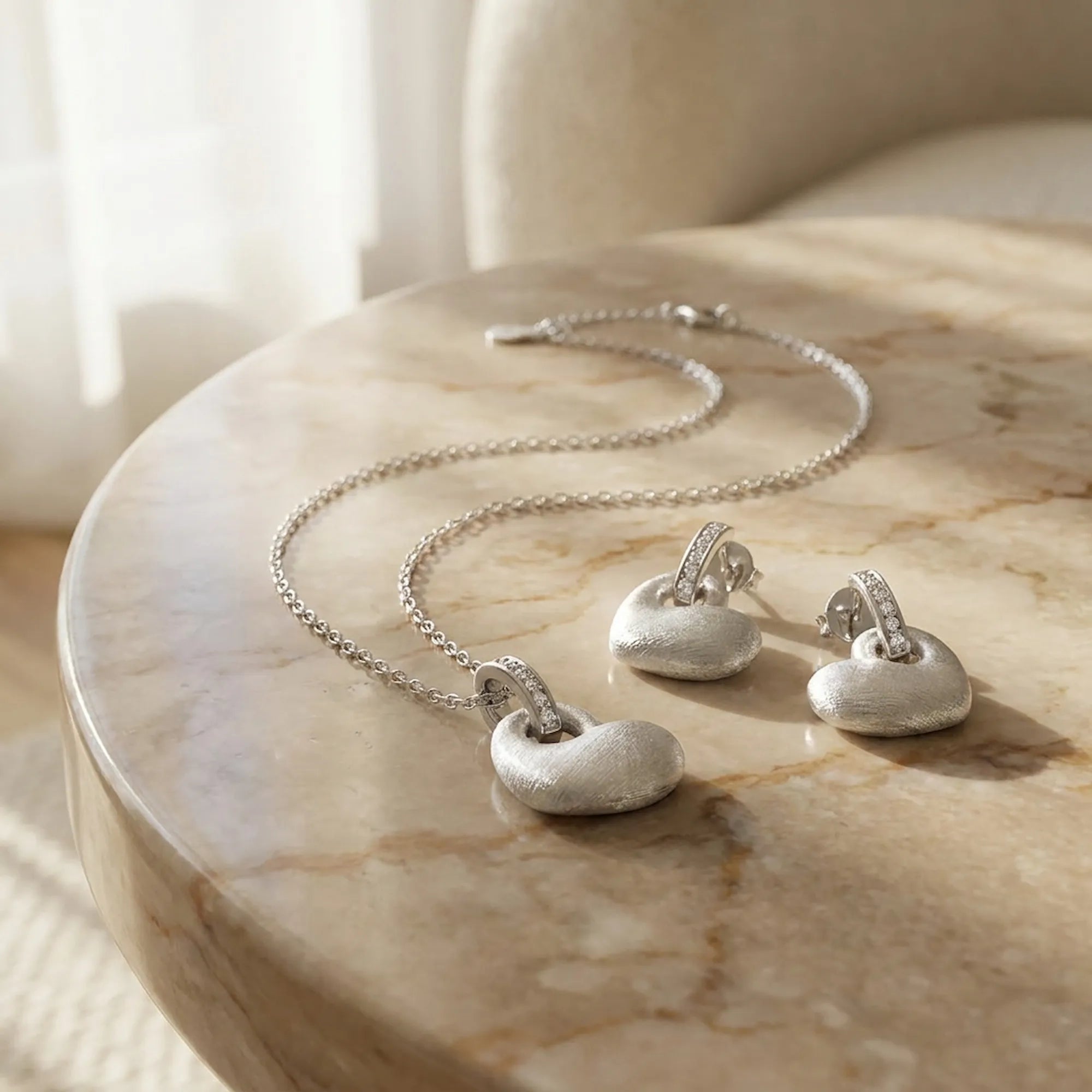 Rhodium silver puffed heart pendant and drop earring set on marble surface — editorial gifting display Dubai