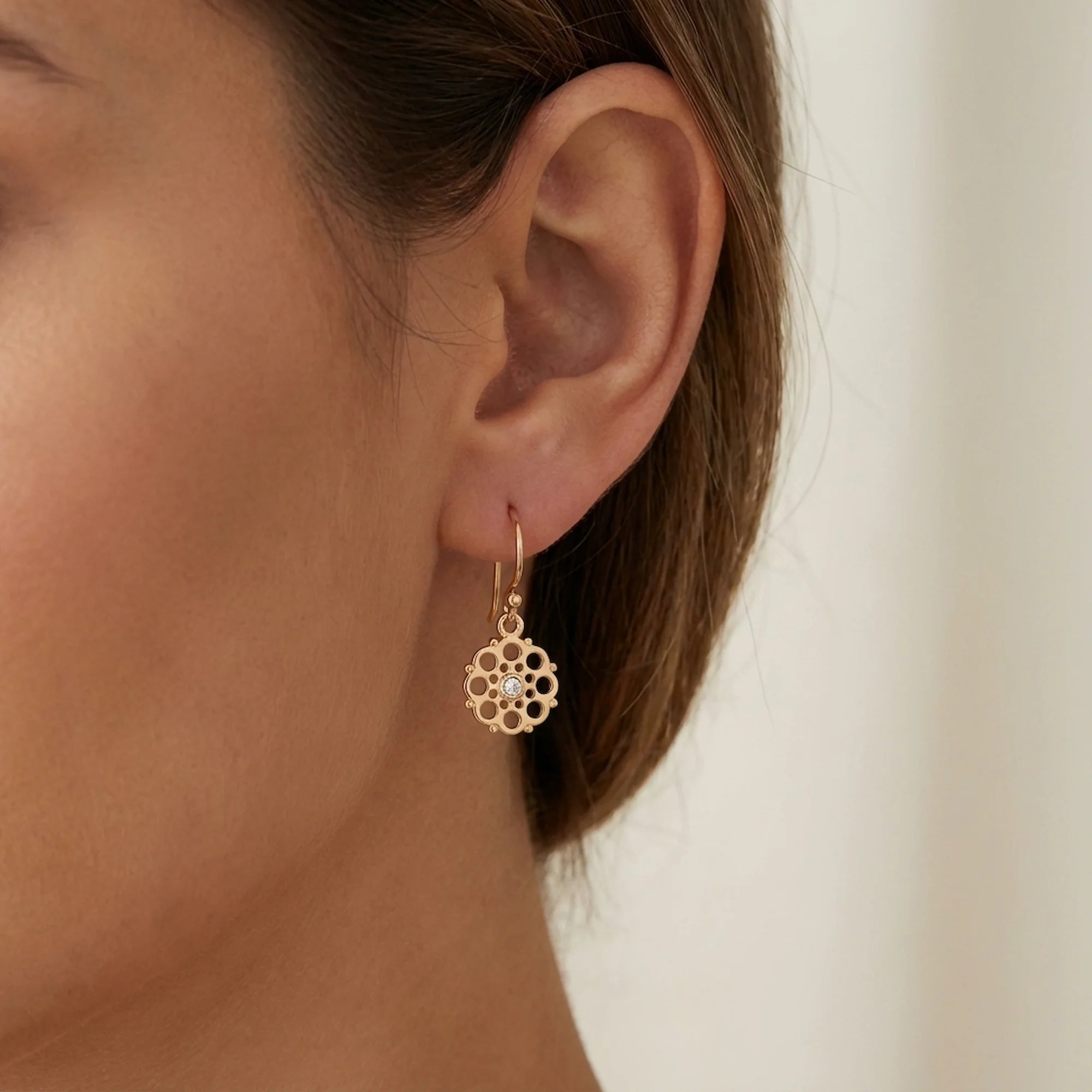 Woman indoors in Dubai wearing gold vermeil radial pierced-disc drop earrings with cubic zirconia.