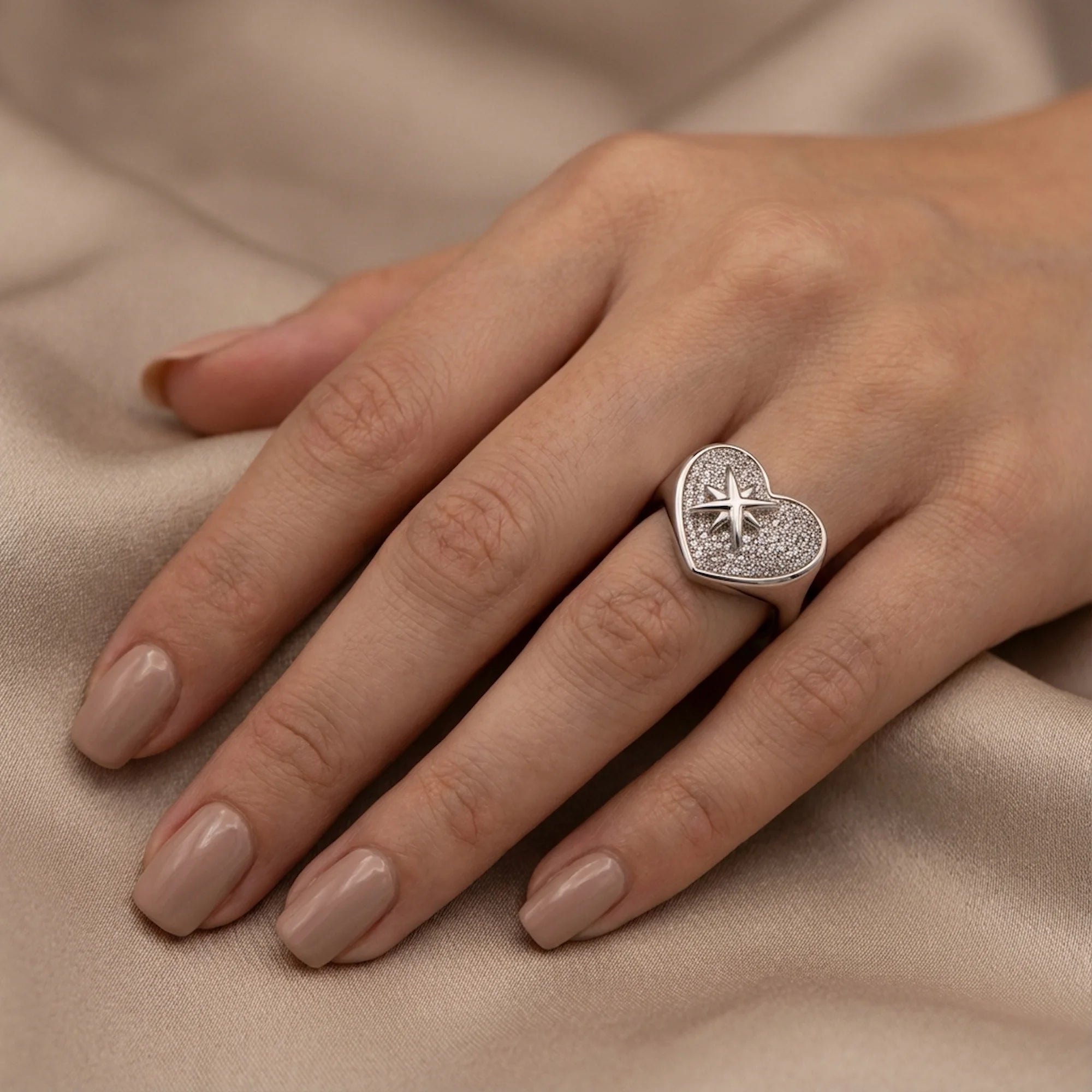 Hand wearing rhodium plated 925 silver pavé heart ring with cubic zirconia resting on silk in Dubai.