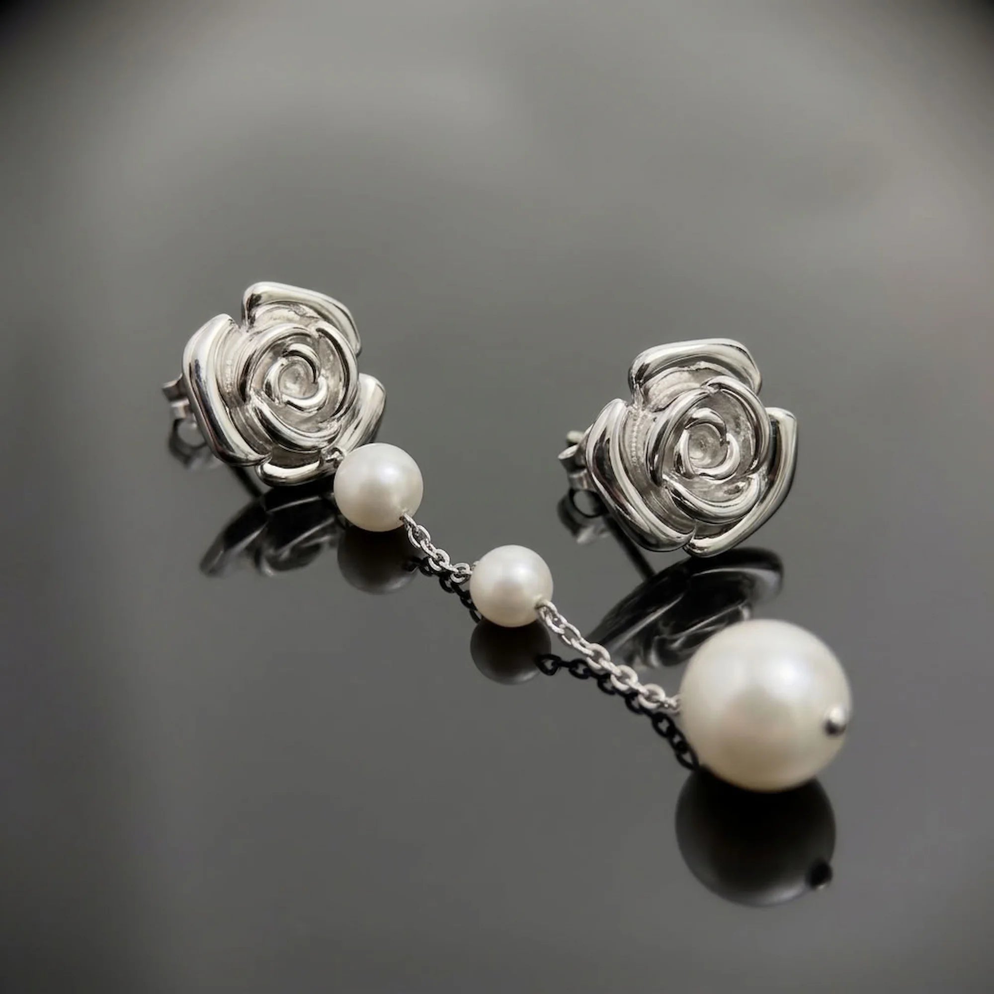 Rhodium-plated 925 silver sculpted rose stud earrings with an attached faux pearl chain drop in Dubai.