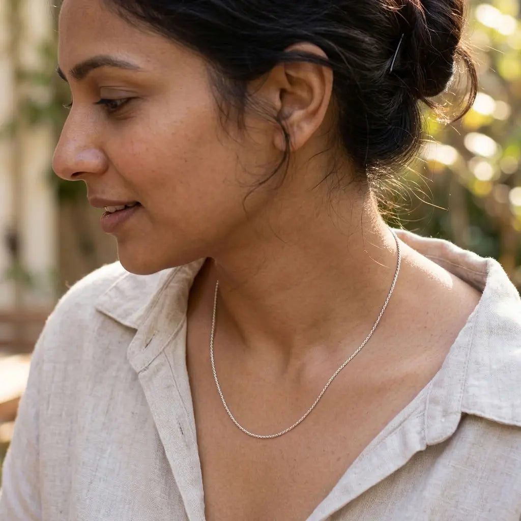 Woman wearing a fine silver-tone rope-style necklace with a cream collared shirt.
