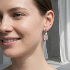 Close-up of natural rose quartz teardrop earring worn on ear — pale blush translucent stone and 925 silver bail detail