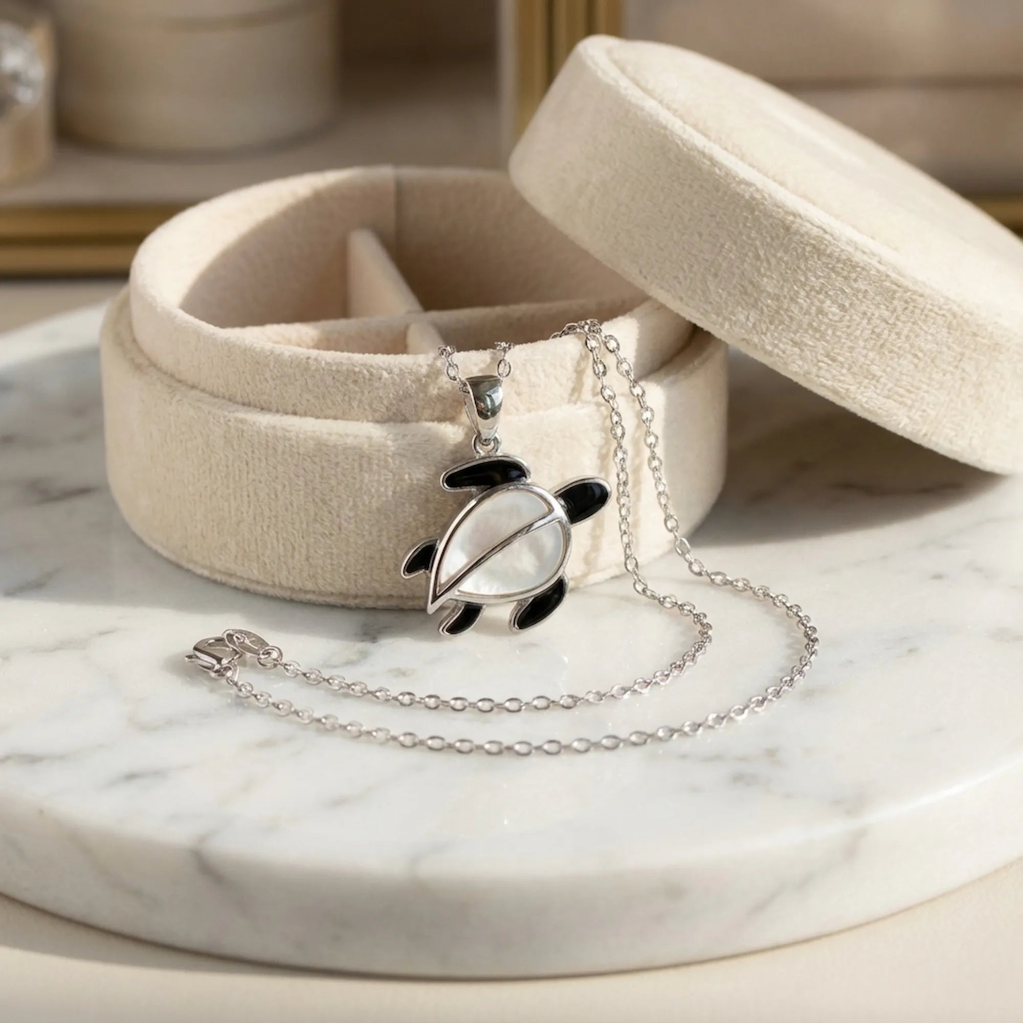 Sea turtle silver necklace with Mother of Pearl shell draped over open cream velvet Luna Dura gift box on white marble