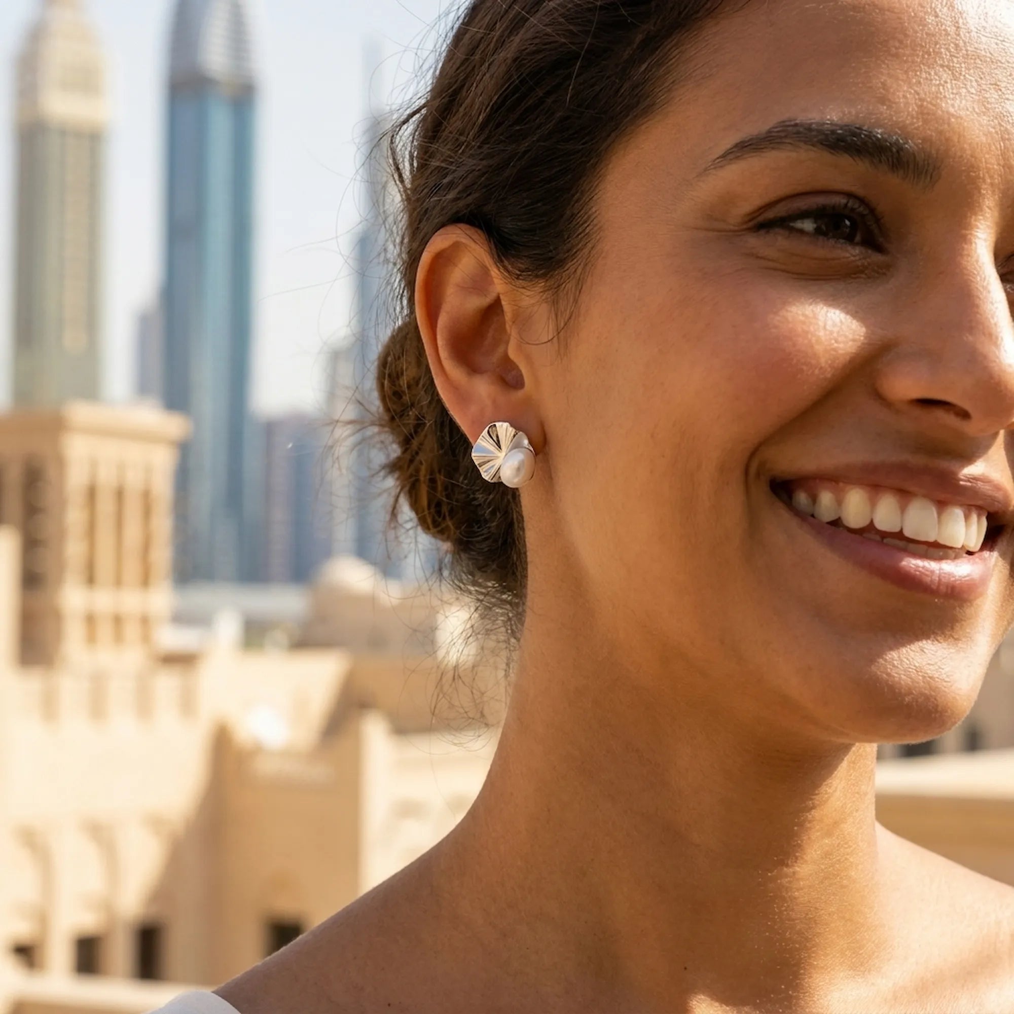 Woman wearing shell pearl stud earrings with Dubai heritage architecture and skyline in the background