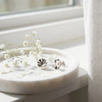 Shell pearl rhodium silver stud earrings on marble dish with white gypsophila flowers in natural light