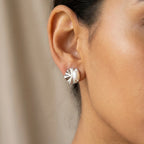 Close-up of shell pearl stud earring on ear against neutral draped fabric, rhodium fan shell detail
