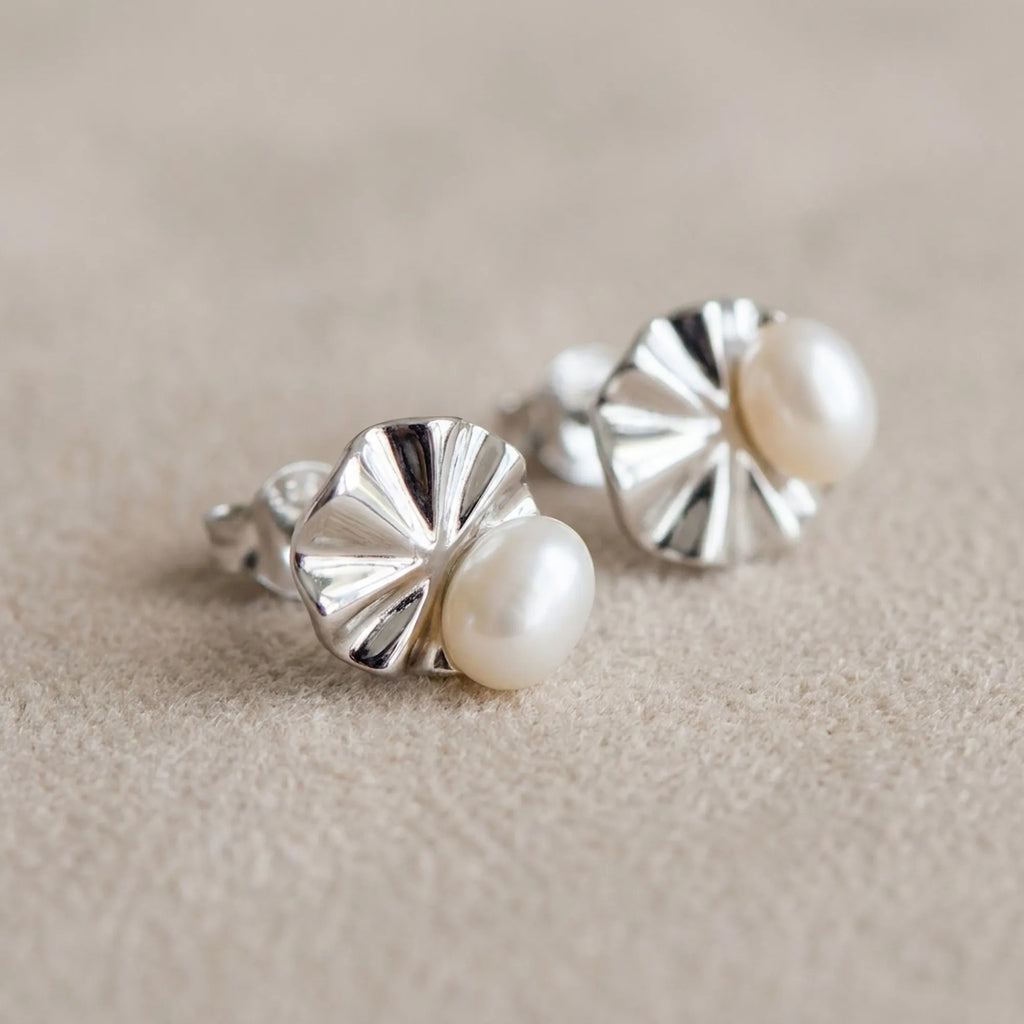 Macro detail of shell pearl stud earrings on linen showing ridged fan motif and lustrous pearl centre