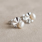 Macro detail of shell pearl stud earrings on linen showing ridged fan motif and lustrous pearl centre