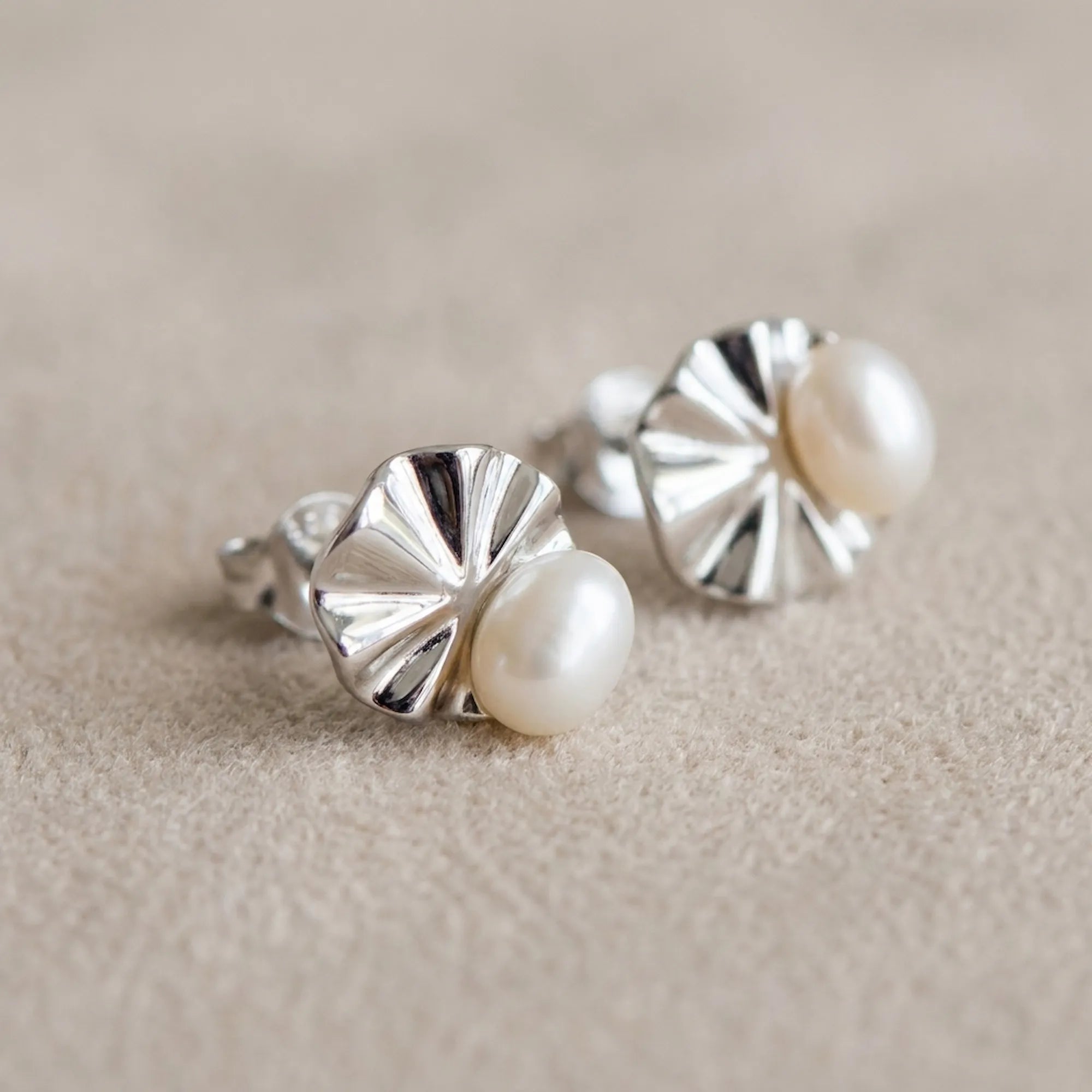 Macro detail of shell pearl stud earrings on linen showing ridged fan motif and lustrous pearl centre