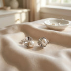 Shell pearl stud earrings resting on draped cream satin fabric in warm natural light, rhodium finish