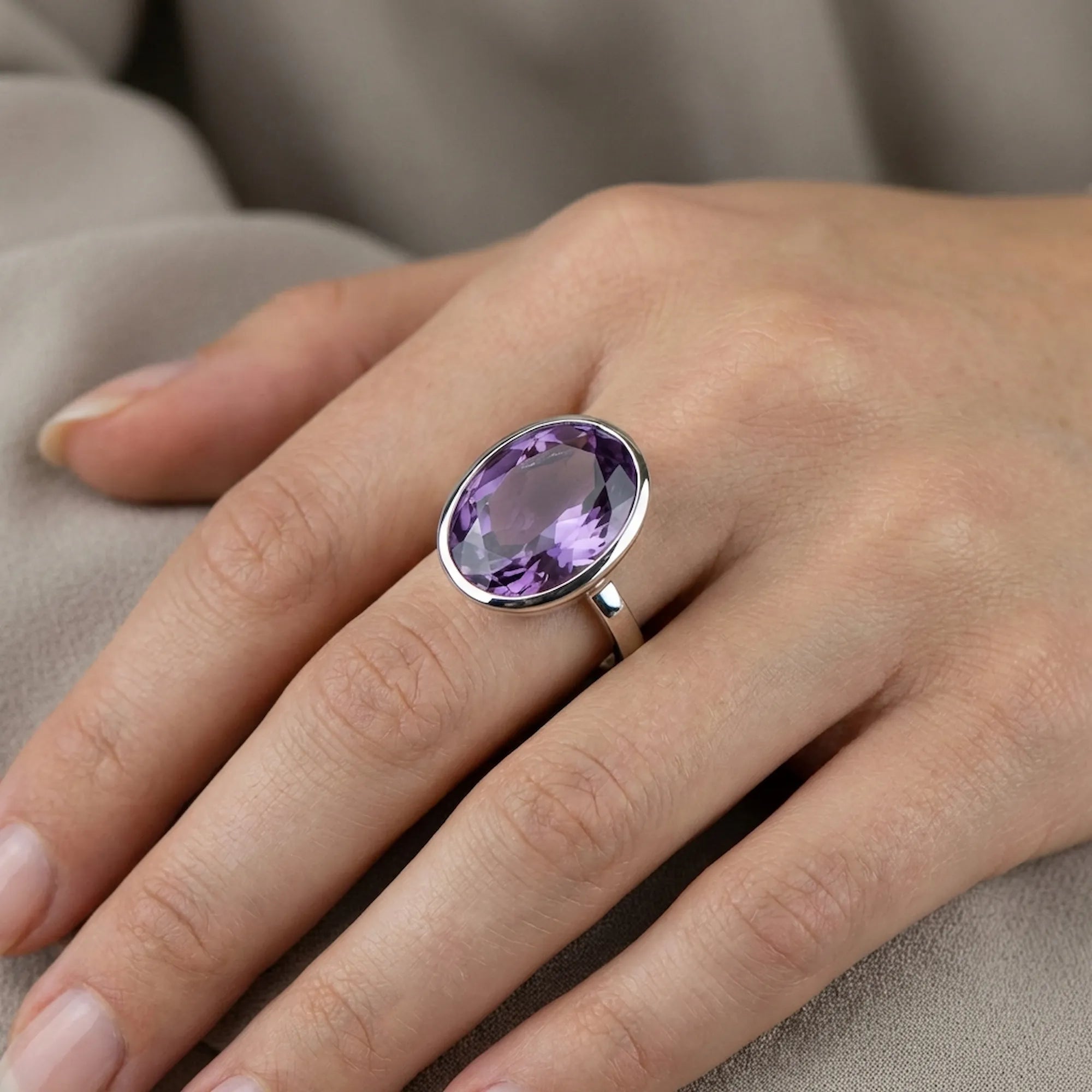 Macro close-up of a deep purple oval cut amethyst highlighting its internal faceting and the seamless silver bezel edge.