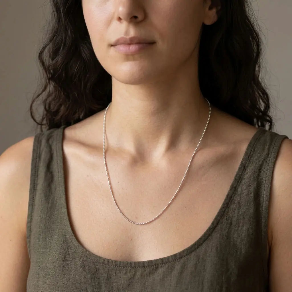 Woman wearing a delicate silver-tone ball chain necklace with an olive sleeveless top.