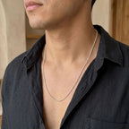 Man wearing a fine silver-tone bead chain necklace with a dark collared shirt.
