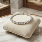 High-shine silver-tone tennis bracelet with brilliant-cut CZ stones draped over a cream velvet display pillow in a boutique setting