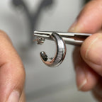 Close up of a ribbed 925 sterling silver crescent moon hoop earring held by tweezers in Dubai.