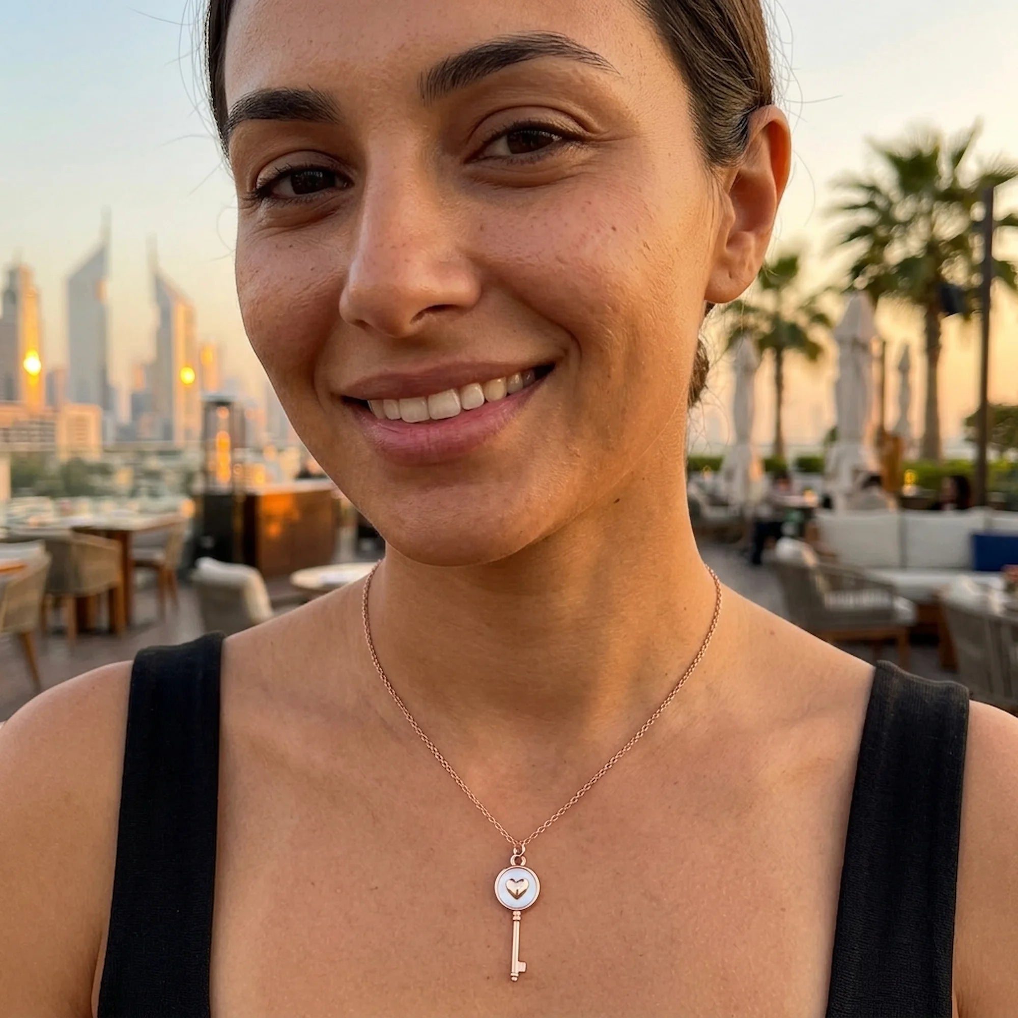 Woman smiling outdoors in Dubai wearing a rose gold plated 925 sterling silver heart-and-key necklace.