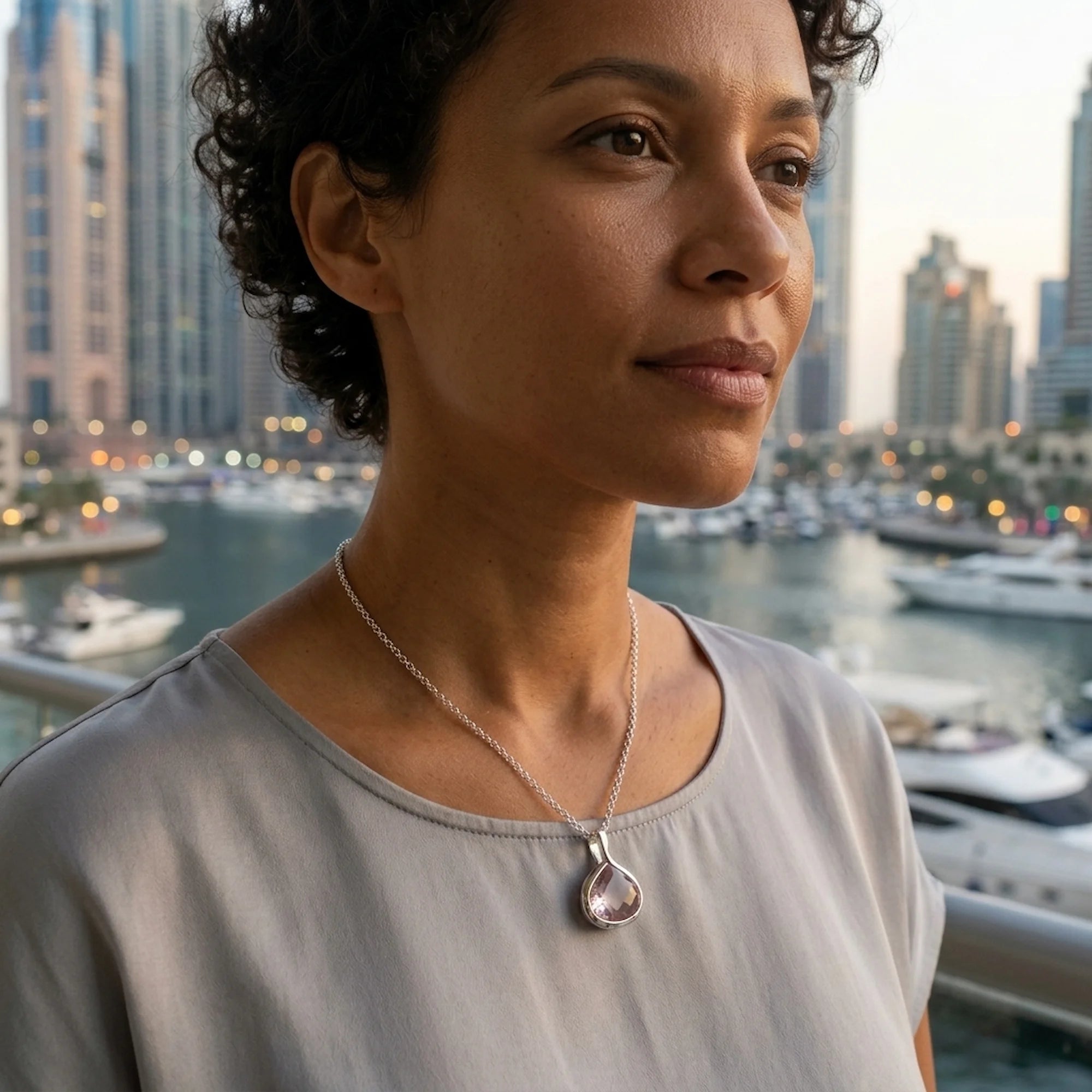 Woman wearing the 925 sterling silver natural rose quartz lotus pendant necklace against the Dubai Marina skyline UAE.