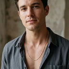 Man wearing a fine silver-tone station-link necklace with a charcoal open-collar shirt.