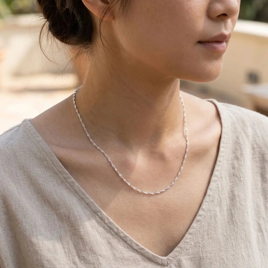 Woman wearing a bright twisted-link silver-tone chain necklace with a beige V-neck top.