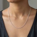 Woman wearing a fine twisted silver-tone Singapore-style necklace with a charcoal neckline.