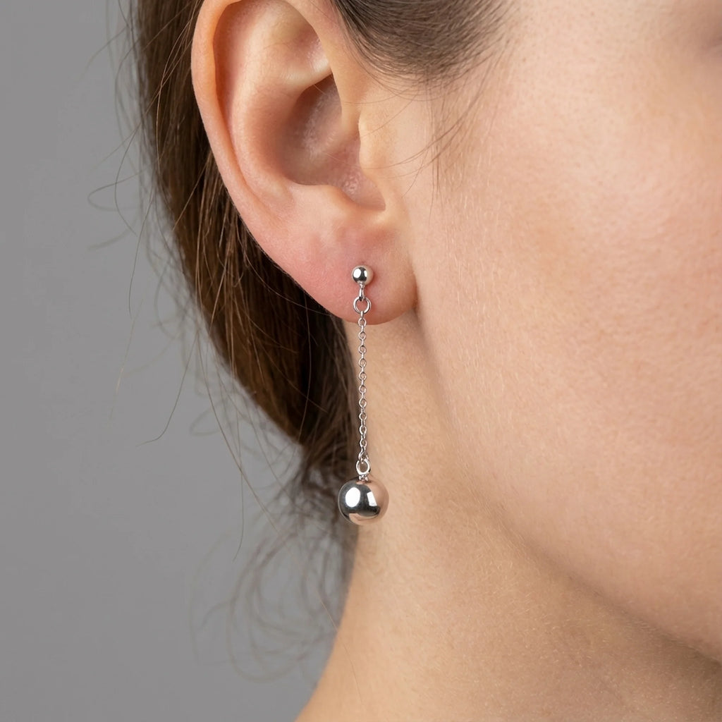 Woman wearing 925 sterling silver chain drop earrings with a polished sphere, outdoors in Dubai.