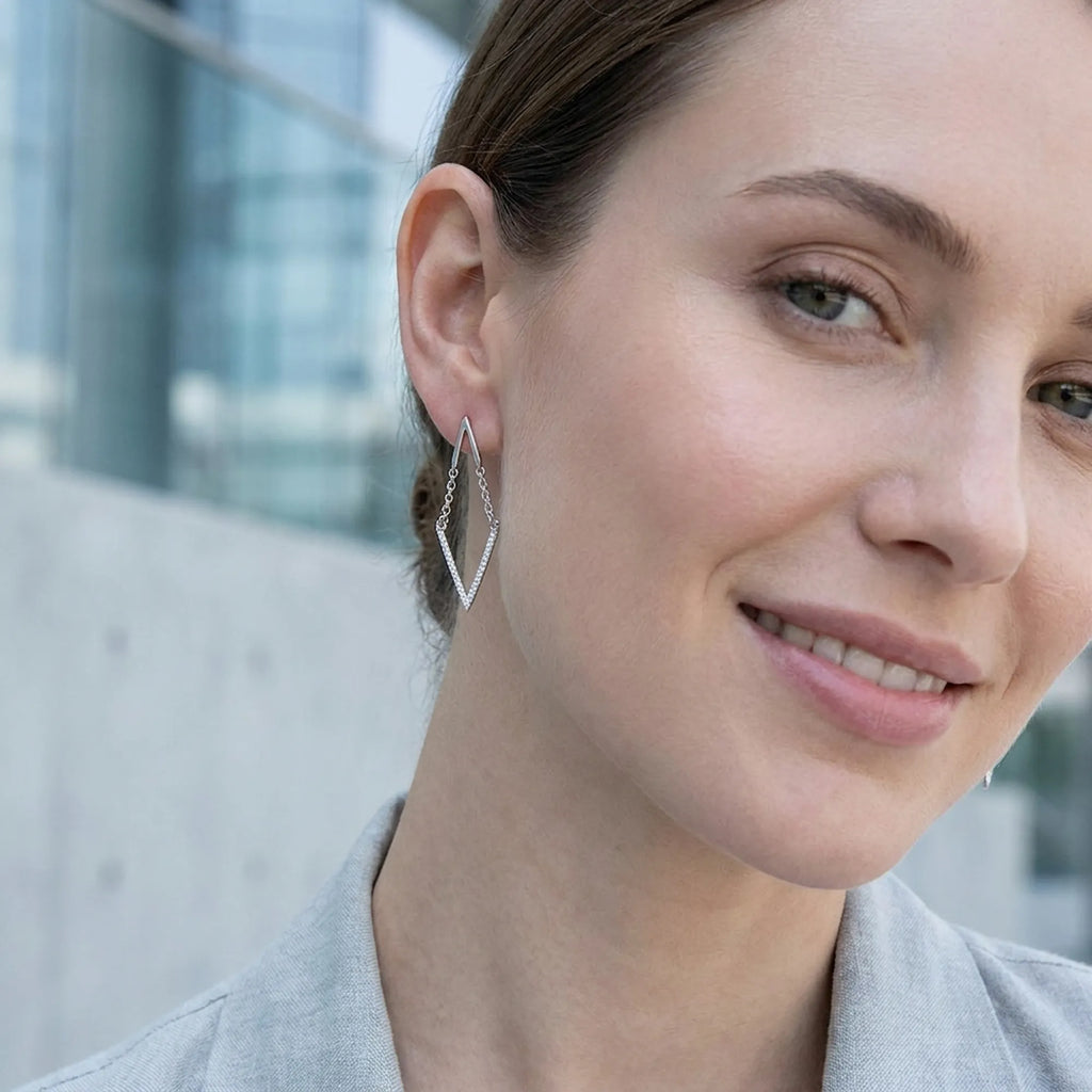 Silver chevron V drop earring on the ear, architectural cool-tone style, DIFC Dubai backdrop