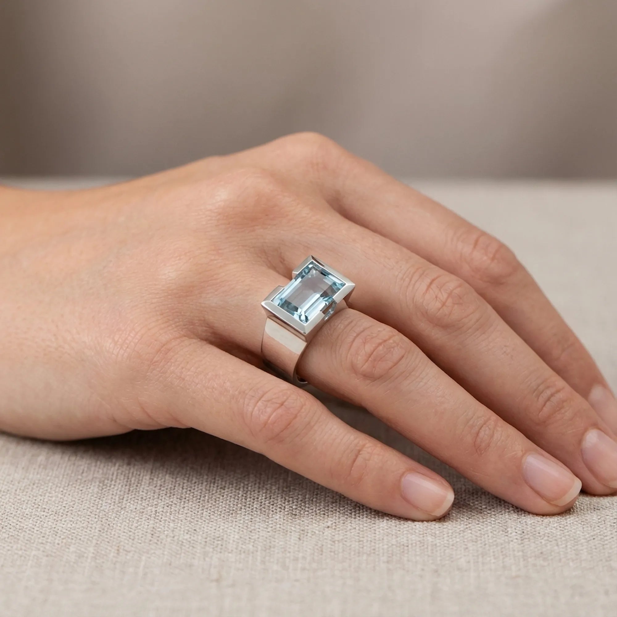 Natural sky blue topaz statement ring worn on hand against linen fabric — 925 sterling silver architectural half-bezel setting
