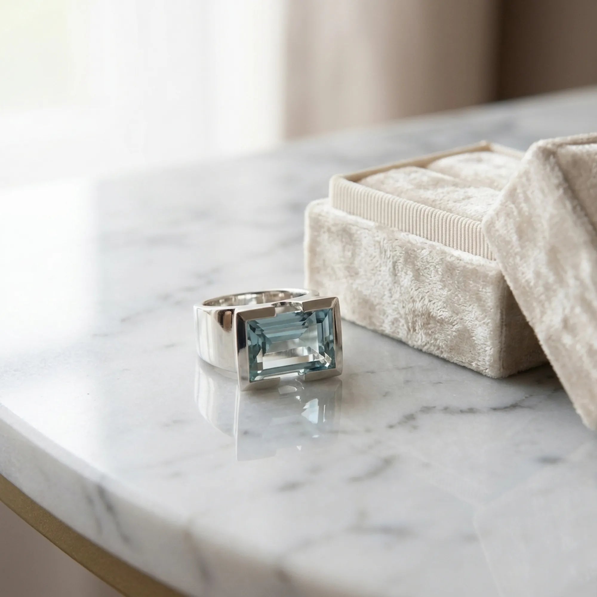 Sky blue topaz 925 silver statement ring on marble surface beside cream velvet gift box — architectural half-bezel detail