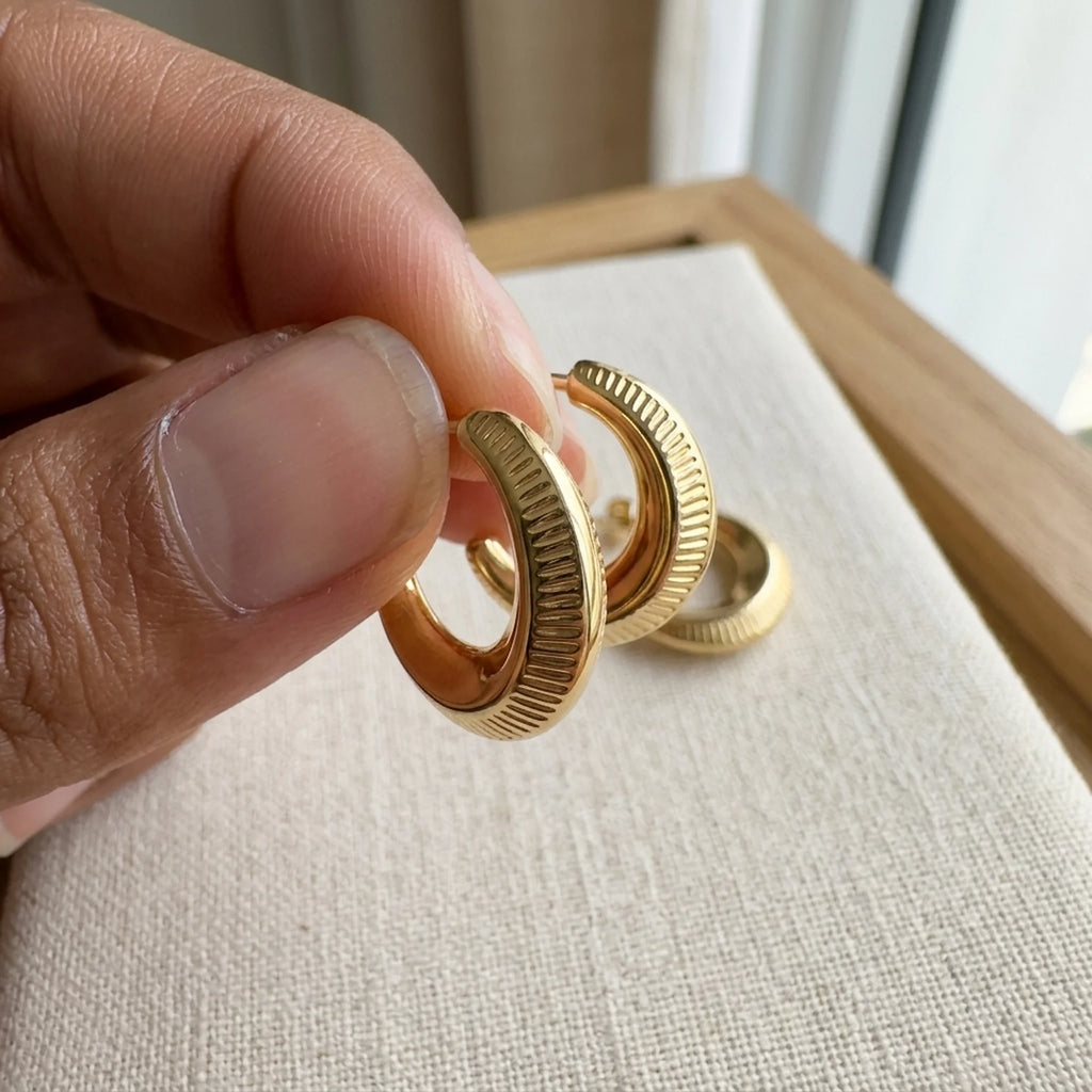 Close up of a ribbed 18K gold vermeil crescent moon hoop earring held between fingers in Dubai.