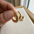 Close up of a ribbed 18K gold vermeil crescent moon hoop earring held between fingers in Dubai.